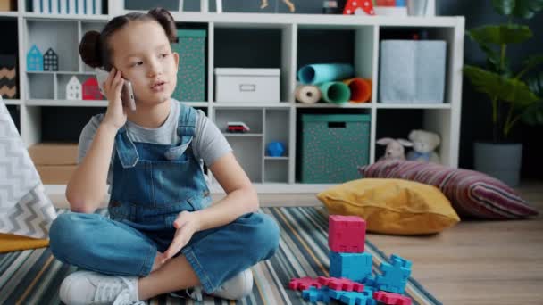 Menina alegre falando no telefone celular sorrindo sentado no chão em quarto de crianças — Vídeo de Stock