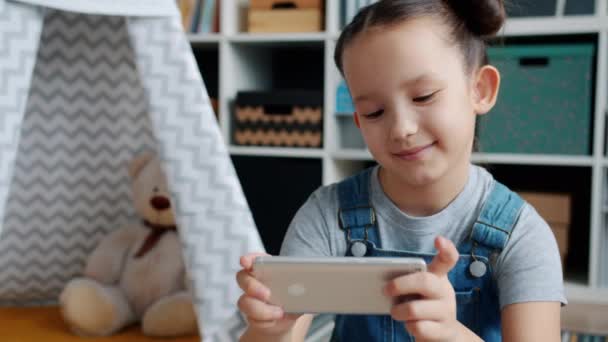 Criança alegre jogando videogame com smartphone desfrutando de nova aplicação dentro de casa — Vídeo de Stock