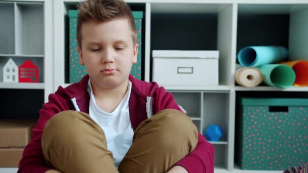 Portret van een verdrietig kind dat thuis op de vloer zit en zich verveelt en ongelukkig voelt — Stockvideo