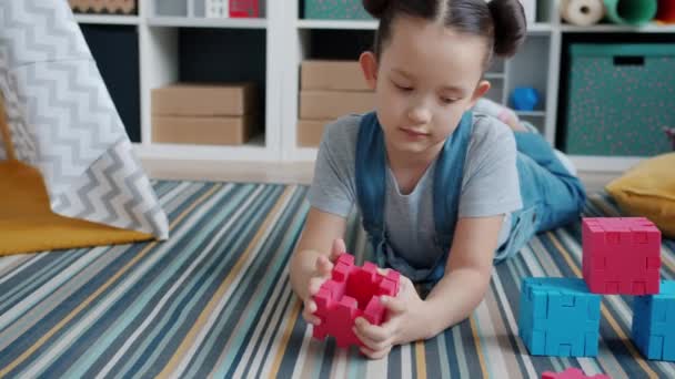 Bonito menina brincando com brinquedos coloridos apreciando jogo deitado no tapete no quarto — Vídeo de Stock