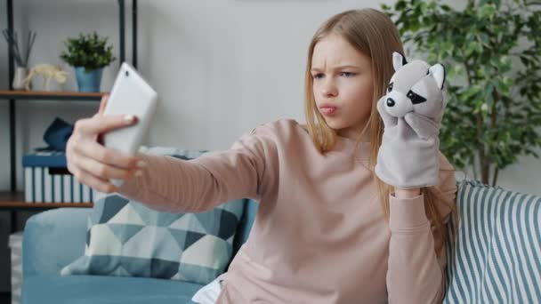 Радісна дитина бере селфі з рукавичками маріонетка позує на камеру смартфона, розважаючись вдома — стокове відео