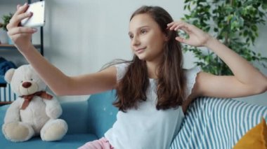 Çekici kız akıllı telefonuyla özçekim yapıyor. Kameraya poz veriyor. Evde saça dokunuyor.