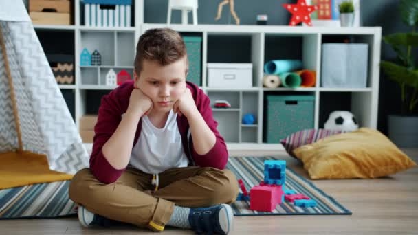 Повільний рух самотньої дитини, що сидить на підлозі в ігровій кімнаті, відчуває себе нещасним і нудним — стокове відео