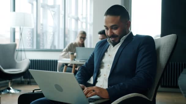 Beau entrepreneur arabe utilisant un ordinateur portable travaillant à l'intérieur dans le hall de l'hôtel avec un groupe de personnes en arrière-plan — Video