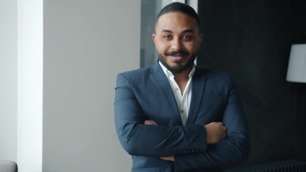Langsom bevegelse av kjekk arabisk forretningsmann i dress som står på kontoret og smiler til kameraet – stockvideo