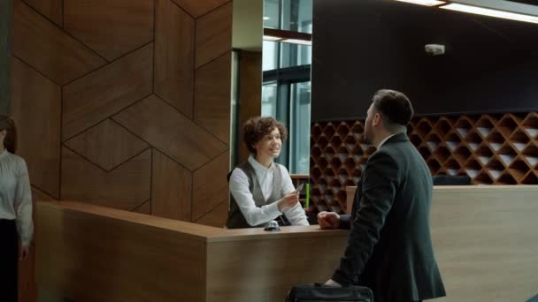 Чоловік гість розмовляє з адміністратором готелю і отримує ключову картку під час прогулянки чоловіком і жінкою — стокове відео
