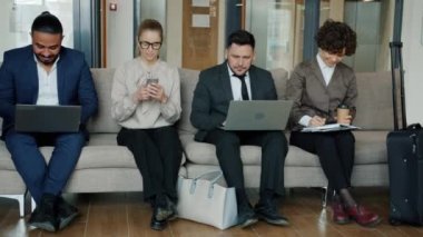 Otel lobisinde çalışan bir grup insan bilgisayar ve akıllı telefon kullanıyor.
