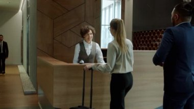 Otel resepsiyonisti misafirleri karşılıyor iş adamlarıyla konuşuyor ve anahtar kartları veriyor.