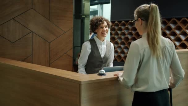 Hoteladministrateur begroet klanten bij de check-in balie geven sleutelkaarten praten glimlachend — Stockvideo