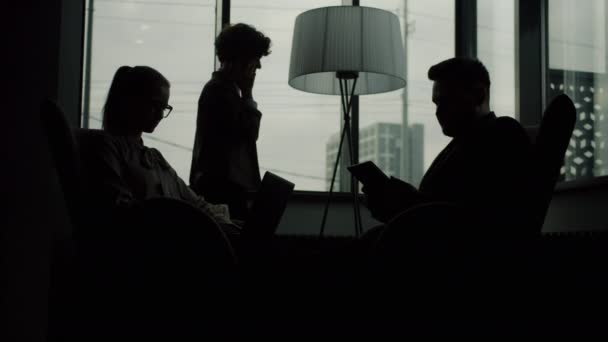 Silhouettes d'hommes et de femmes travaillant dans un bureau sombre utilisant des appareils parlant et faisant des appels téléphoniques — Video