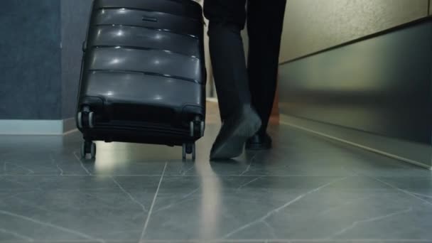 Cámara lenta de tiro bajo de piernas masculinas caminando en el vestíbulo del hotel moviendo la maleta yendo a la habitación — Vídeos de Stock