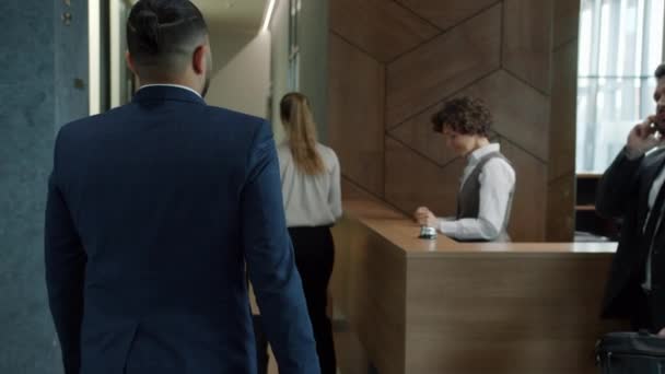 Śledzenie ujęcia biznesmena z Bliskiego Wschodu przybywającego do hotelu, rozmawiającego z menedżerem, który dostaje kartę z bagażem. — Wideo stockowe