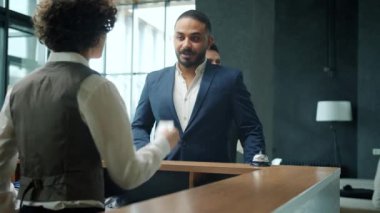 Çok ırklı iş adamları otele giriş yapıyor. Resepsiyonistle konuşup anahtar kartı alıyorlar.
