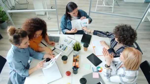 Gruppo di donne che condividono idee imprenditoriali scambiandosi carte con grafici seduti alla scrivania insieme — Video Stock