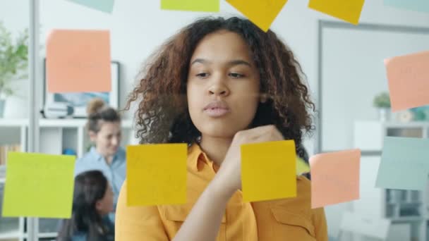 कार्यालय में रंगीन चिपकने वाले नोटों के साथ काम करने वाले सुंदर अफ्रीकी अमेरिकी कर्मचारी की धीमी गति — स्टॉक वीडियो