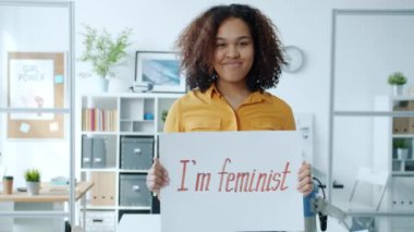 İçerde tek başına gülümseyen, feminist bayrak tutan neşeli Afrikalı Amerikalı kızın portresi.