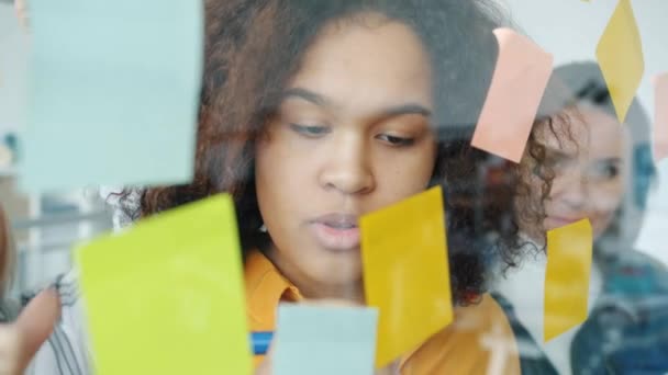 Primer plano de la mujer afroamericana escribiendo en notas adhesivas y discutiendo ideas con un equipo multiétnico — Vídeo de stock