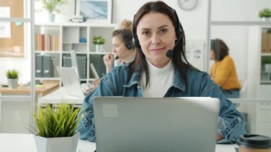 Çağrı merkezi çalışanının portresi modern işyerinde kulaklıklar ve dizüstü bilgisayarla oturuyor.