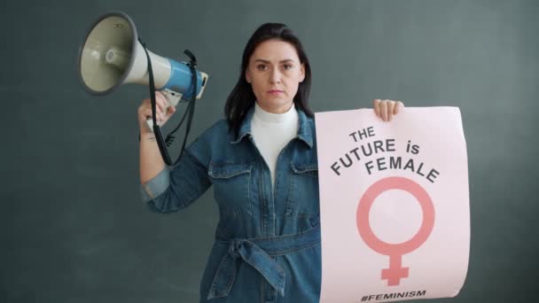 Gri arka planda duran megafon ve afiş tutan kadın aktivistin portresi — Stok video