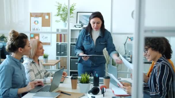 Glada affärskvinna talar med grupp av anställda ger papper under mötet på arbetsplatsen — Stockvideo