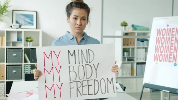 Retrato em câmera lenta de mulher asiática atraente em pé com cartaz feminista no escritório moderno — Vídeo de Stock