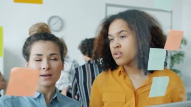 Cam tahtada Afro-Amerikan ve Asyalı meslektaşlar yazıyor ve yapışkan notlarla çalışıyorlar