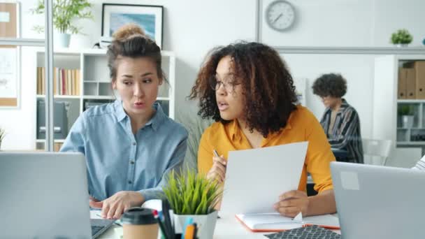 Groupe multi-ethnique de dames discutant du projet regardant les papiers et l'écran d'ordinateur portable travaillant dans le bureau moderne — Video