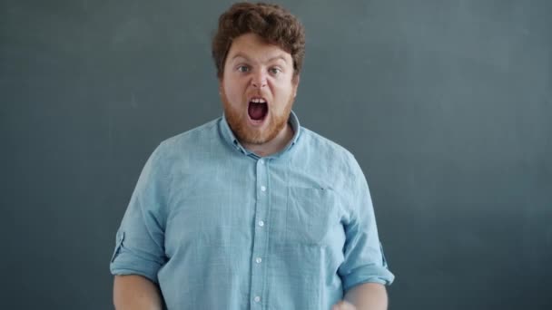 Mouvement lent de la personne excitée exprimant des émotions positives et criant en regardant la caméra sur fond gris — Video