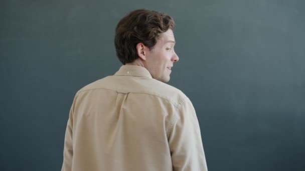 Retrato de um jovem bonito girando e sorrindo olhando para a câmera em fundo cinza — Vídeo de Stock