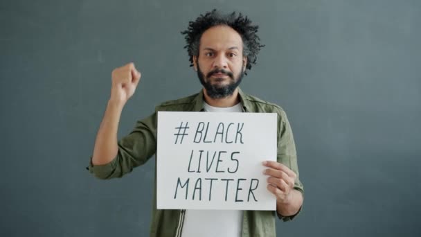 Aktivist einer gemischten Rasse hält ein Poster von Black Lives Matter im Kampf gegen Rassismus vor grauem Hintergrund — Stockvideo