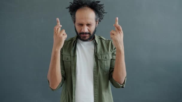 Ritratto al rallentatore dell'uomo arabo di mezza età che esprime un desiderio con le dita incrociate su sfondo grigio — Video Stock