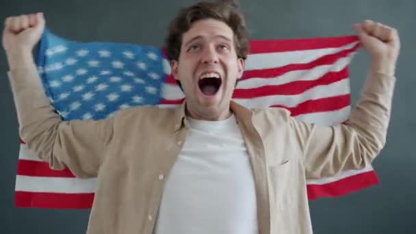 Lento retrato movimento de feliz cidadão dos EUA gritando e acenando bandeira americana em fundo cinza — Vídeo de Stock