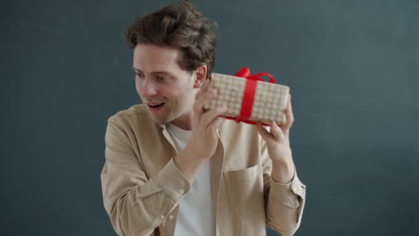 Медленный портрет веселого парня, трясущего подарочной коробкой, наслаждающегося подарком и сюрпризом — стоковое видео