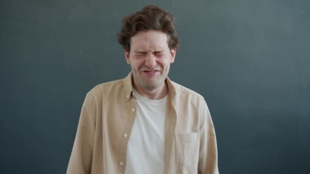 Verspielter Typ mit lustigen Grimassen und Gesten, der auf grauem Hintergrund in die Kamera schaut — Stockvideo