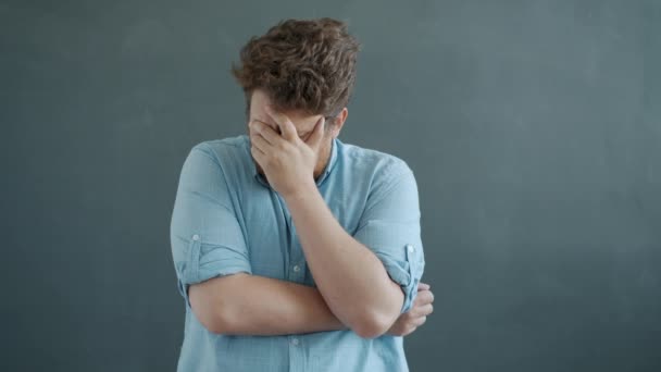 Retrato de câmera lenta de cara infeliz expressando emoções negativas, em seguida, coçar a barba no fundo cinza — Vídeo de Stock