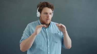 Dikkatsiz bir adamın portresi. Kulaklıkla müzik dinleyip gri arka planda eğleniyor.