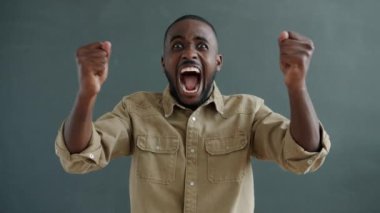 Gri arka planda gülen ve kollarını kaldıran neşeli Afrikalı Amerikalı kişinin portresi