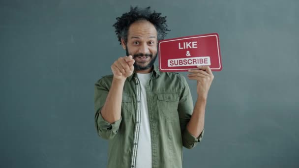 Langzame beweging van de Arabische blogger die naar de camera wijst en Like en Subscribe teken vasthoudt — Stockvideo