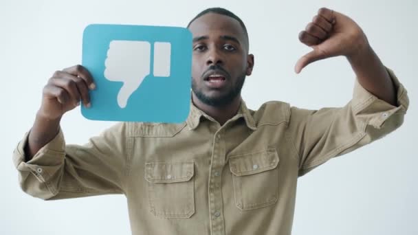 Movimento lento do blogueiro afro-americano masculino segurando sinal de antipatia e fazendo gesto de mão polegar para baixo — Vídeo de Stock