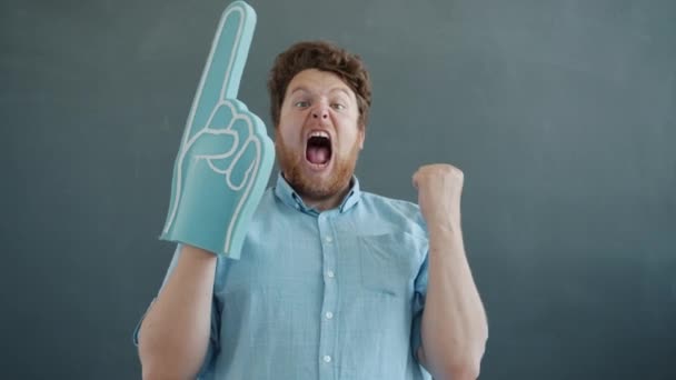 Portrait of guy with foam hand joyful sports fan supporting screaming on gray color background — Stock Video