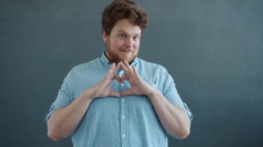 Romantik bir adam kalp şeklinde parmaklar ve öpücüklerle kameraya bakarak flört ediyor.