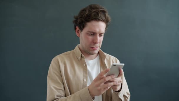 Movimento lento do jovem usando telefone inteligente se comunicando, em seguida, recebendo boas notícias rindo — Vídeo de Stock