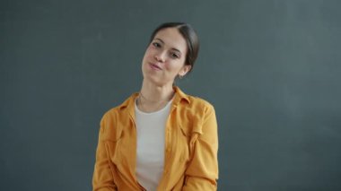 Güzel bir gülümsemeyle kameraya bakan hayalperest genç bir bayanın ağır çekim portresi.