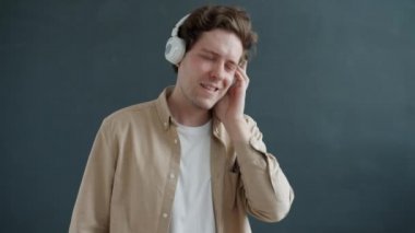 Kulaklıklı ve gri arka planda dans eden, müzikten hoşlanan, kaygısız genç bir adam.