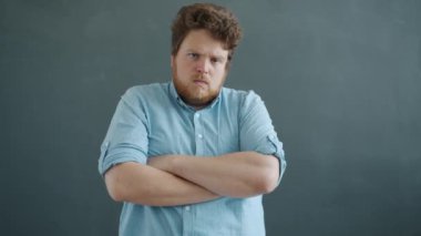 Saldırgan genç adamın kollarını kavuşturup kızgın yüzüyle kameraya bakışının yavaş çekim portresi.