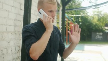 Neşeli genç bir adam cep telefonuyla sohbet ediyor. Yaz günü açık havada gülümsüyor.