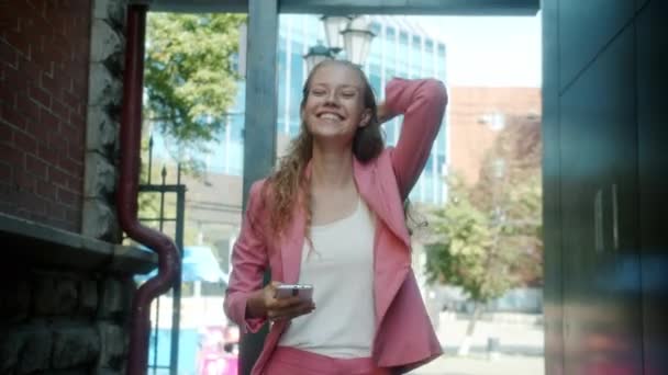 Játékos fiatal nő sétál a város utcájában tánc segítségével okos telefon a nyári napon — Stock videók