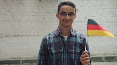 Alman bayrağı tutan ve dışarıda gülümseyen neşeli Orta Doğulu adamın ağır çekimde portresi.