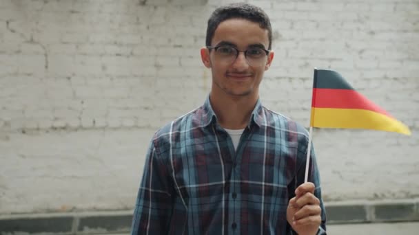 Slow motion portrait of cheerful Middle Eastern man holding German flag and smiling outdoors — Stock Video