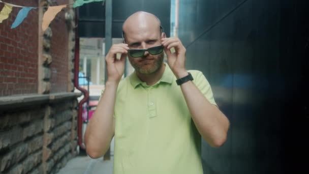 Retrato en cámara lenta de un chico atractivo tocando gafas de sol mirando a la cámara exterior en la calle de la ciudad — Vídeos de Stock
